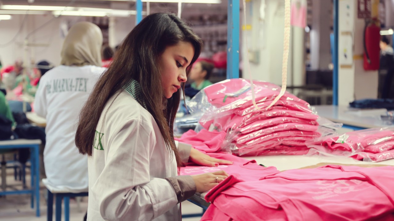 Une jeune femme travaille et examine des t-shirts roses.