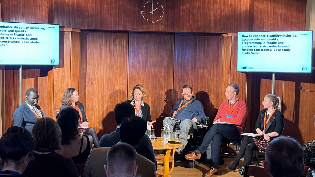 Panel de six personnes, un homme noir, deux hommes blancs et trois femmes blanches. Ils et elles sont assis sur des chaises, l’un des hommes est utilisateur de fauteuil roulant. Ils discutent du sujet suivant : comment renforcer une programmation inclusive du handicap, redevable et de qualité dans les contextes de crise chronique et fragile, en dépit des contraintes financières, le cas du Sud Soudan.