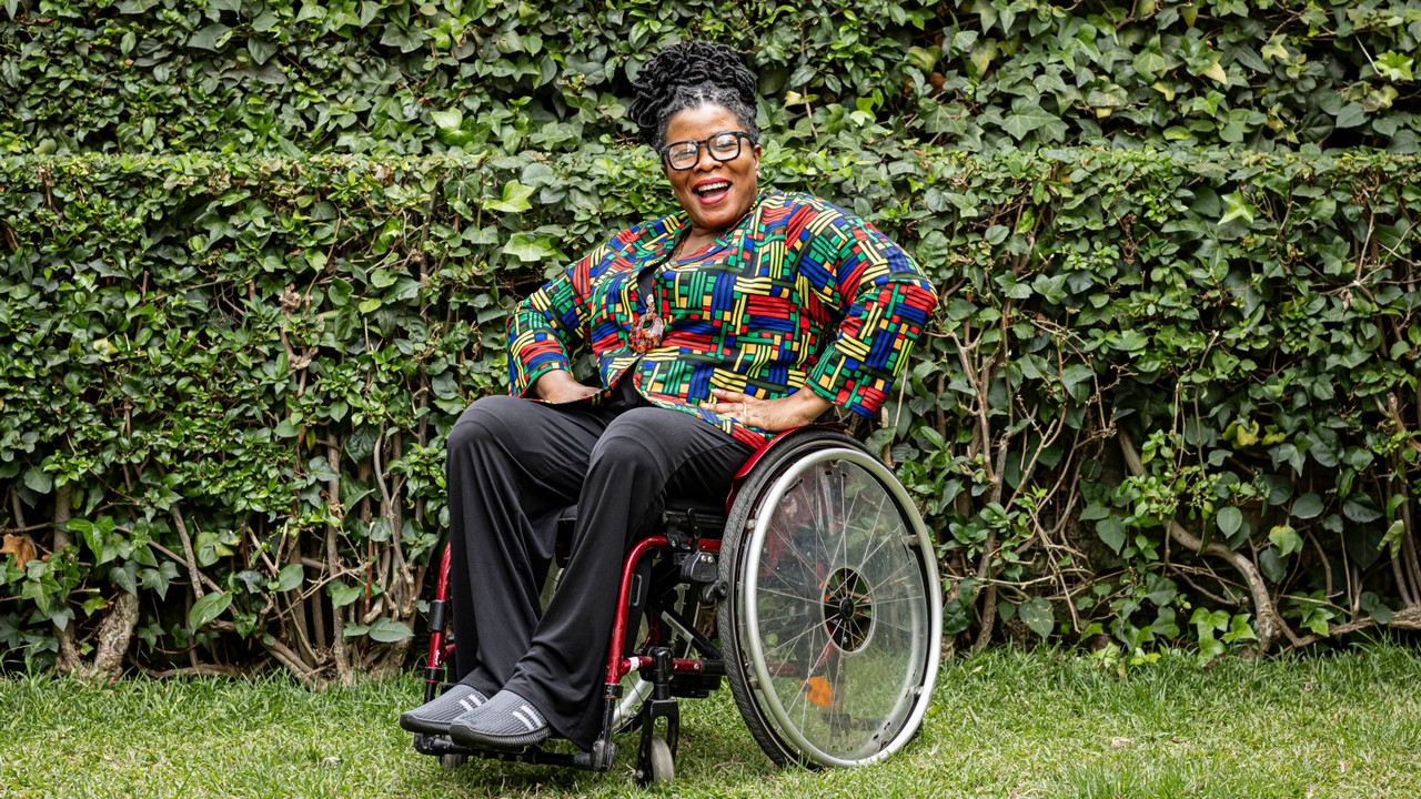 Femme souriante en fauteuil roulant qui pose pour la photo dans un jardin.