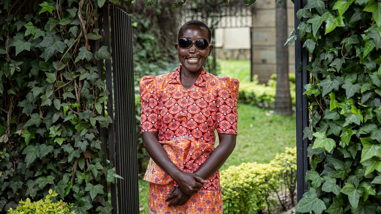 Jeune femme souriante avec des lunettes noires posant dans un jardin.