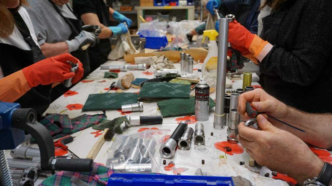 Several people sit around a table cleaning recycled prosthesis components.; }}