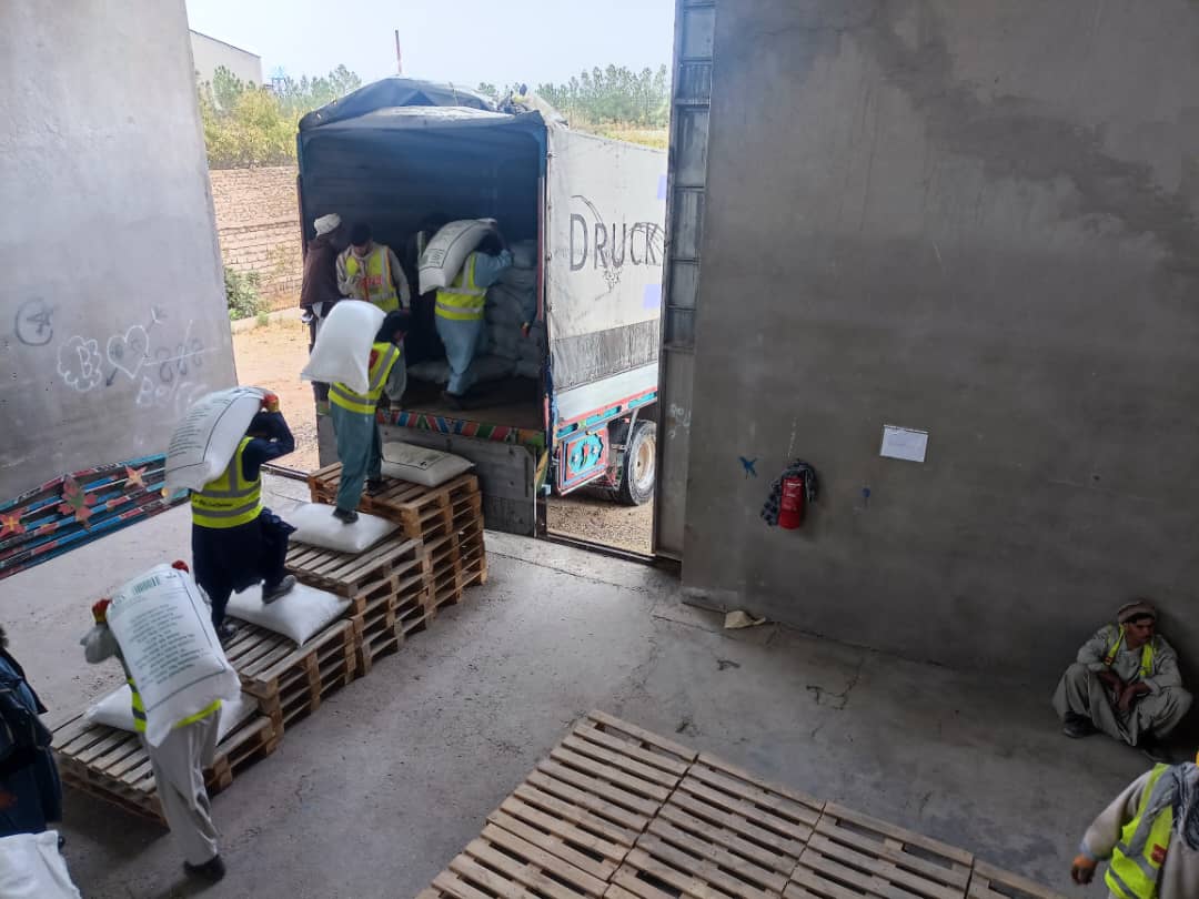 Sur une plateforme de chargement, plusieurs hommes portent de gros sac sur leur dos et les déposent dans un camion.