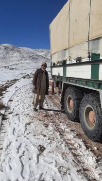 Un homme se tient à côté d'un camion sur une route enneigée.