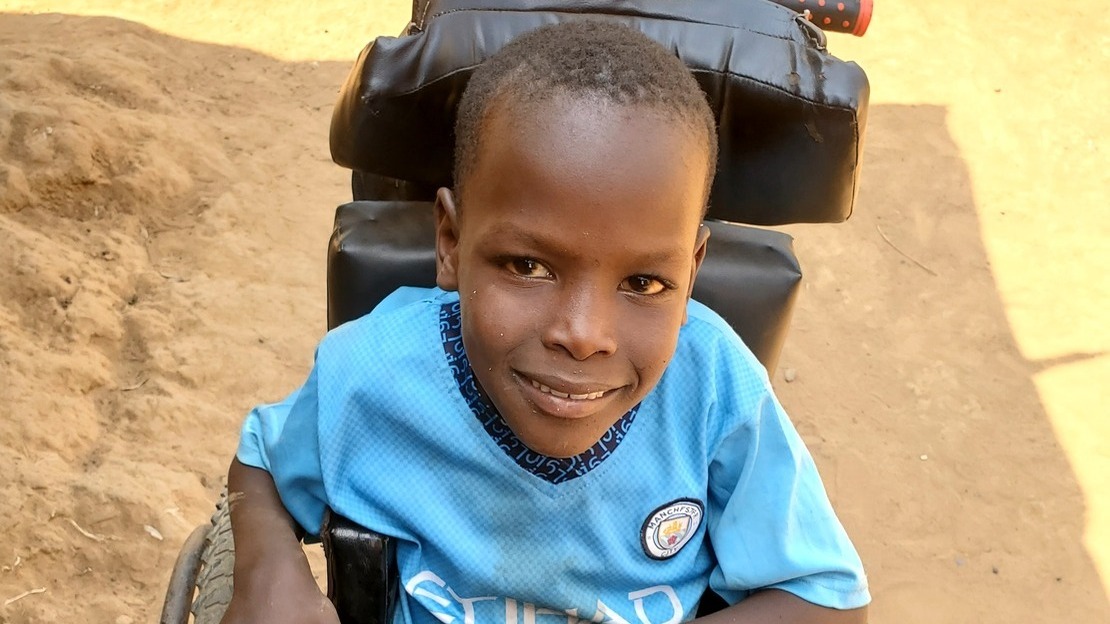 Close-up portrait of a young boy seated in a wheelchair. He looks at the camera and smiles.; }}