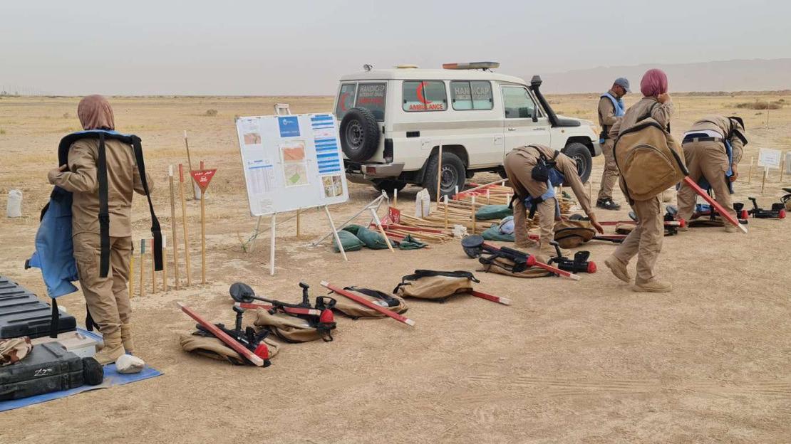 Demining team with their equipment, preparing to leave to clear an area. The team is in a seemingly deserted area.; }}