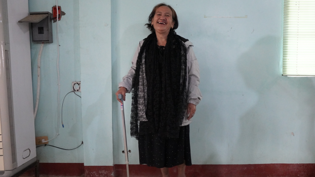 Nanay Benita, 70, received a quad cane from HI as part of its emergency response in the province of Cagayan Nanay Benita is in the centre of the photo, standing with her walking stick and smiling.; }}